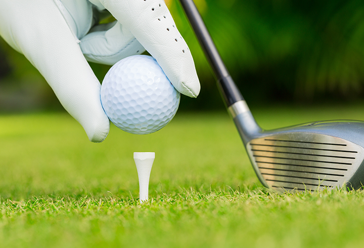 hand placing golf ball on tee to enjoy benefits of playing golf