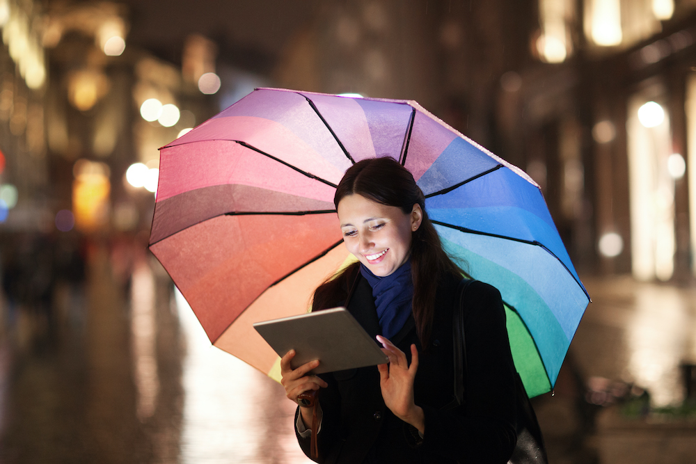 Woman using pad under umbrella in the evening city as she gets weather insurance for insurance brokers and agents