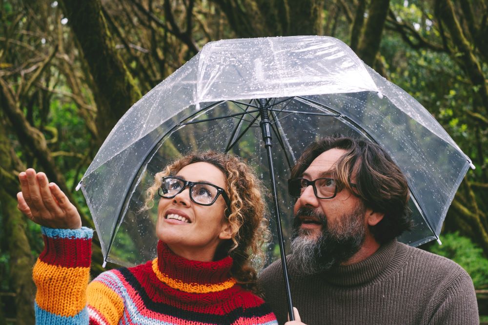 mature couple under umbrella checking weather to see if rained on vs rained out